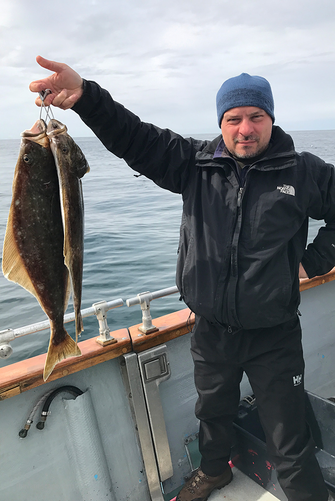 Chris with halibuts in his hand during halibut fishing tour from Homer.