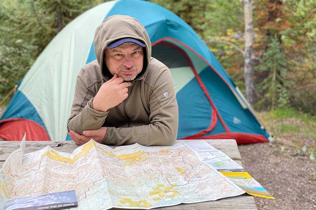 Chris is sitting in front of a tent and analyzing a paper map before we hit hiking trails in the Alaska wilderness.