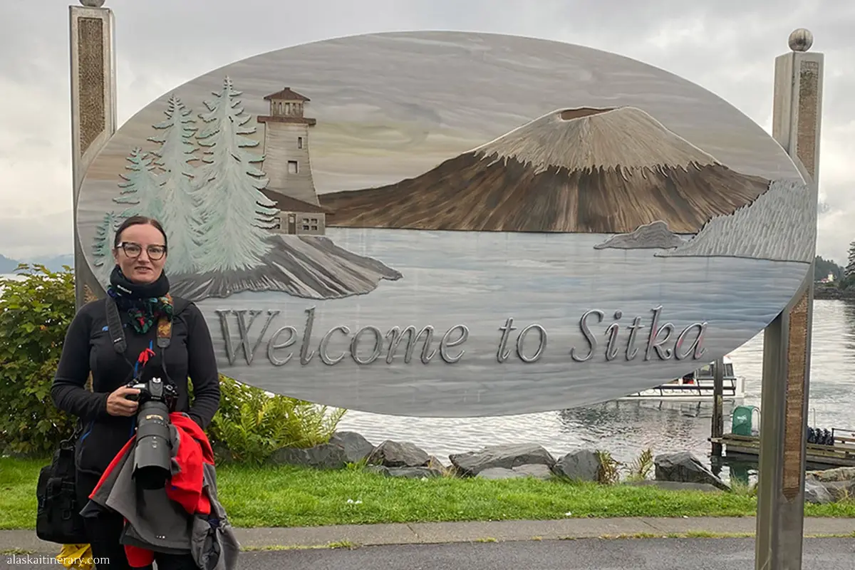 Agnes with a wooden sign Welcome to Sitka.