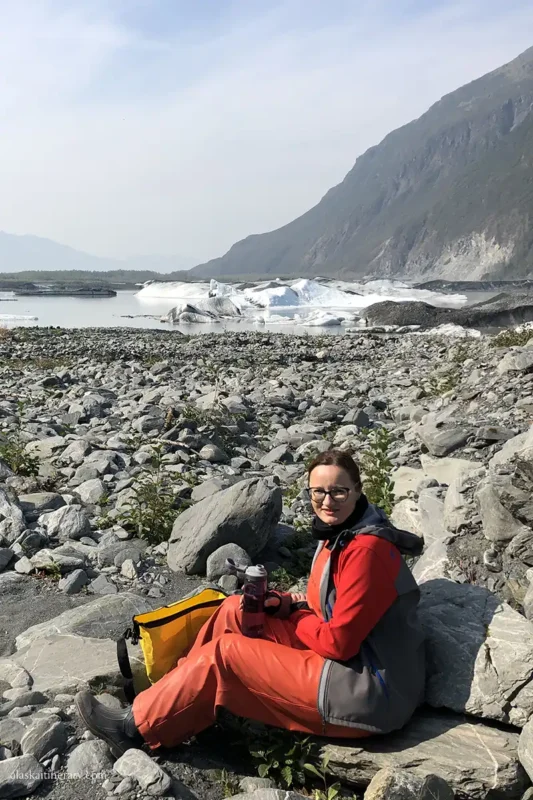 Agnes sitting on rock and drinking water during lunch break with the view at kayak trip, with glacier in the background.