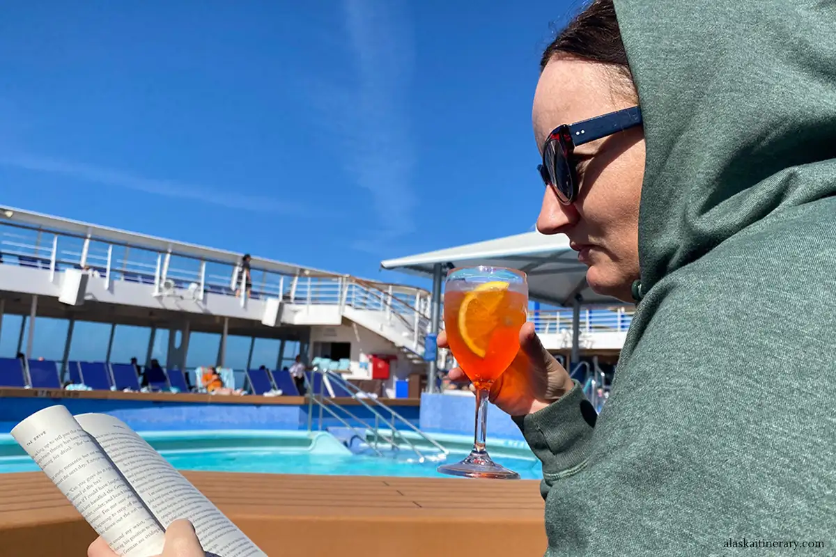 Agnes reading book and drinking coctail next to pool during day at sea on Norwegian Sun ship.