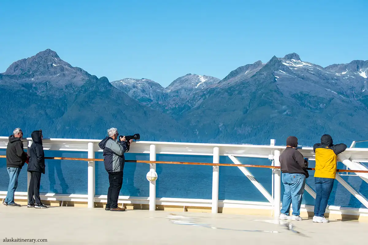 People on the ship dock admiring Alaska landscape wearing windproof jackets and taking pictures.