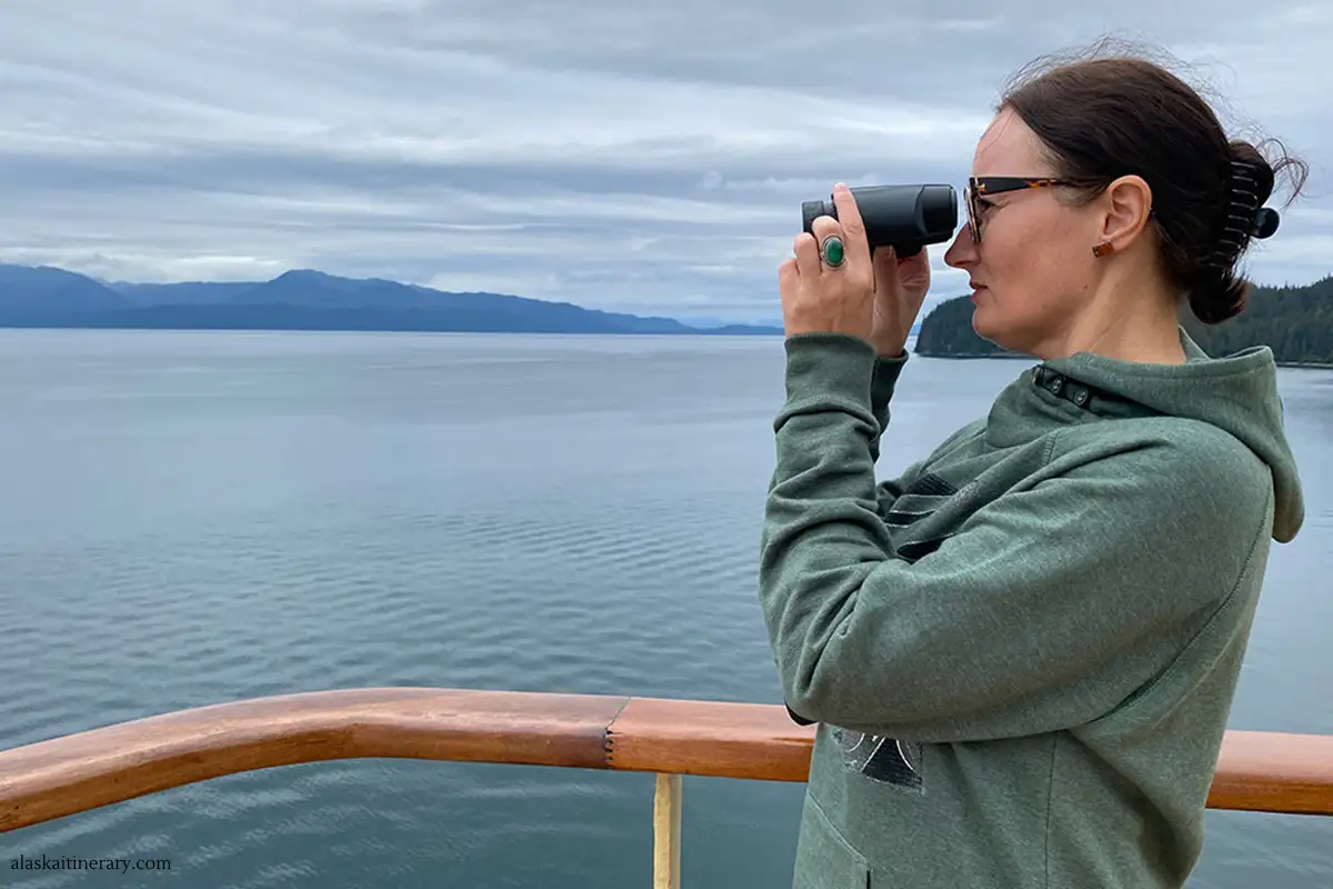 The article's author, Agnes Stabinska, observes the coast and wildlife through binoculars during a shore excursion in Alaska.