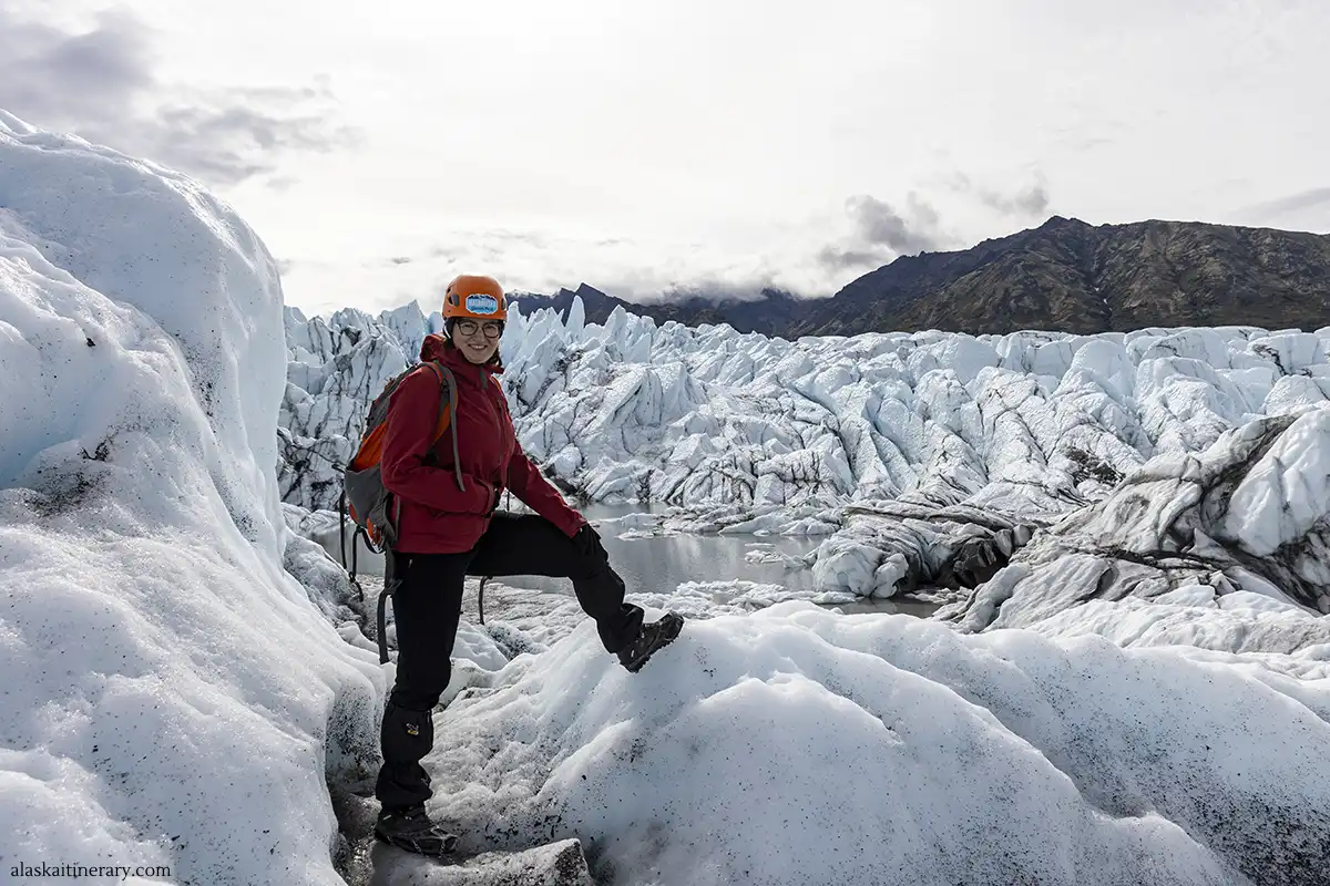 Agnes, equipped with ice gear, smiling on the Matanuska Glacier in Alaska, with intricate ice formations and rugged mountains in the background.
