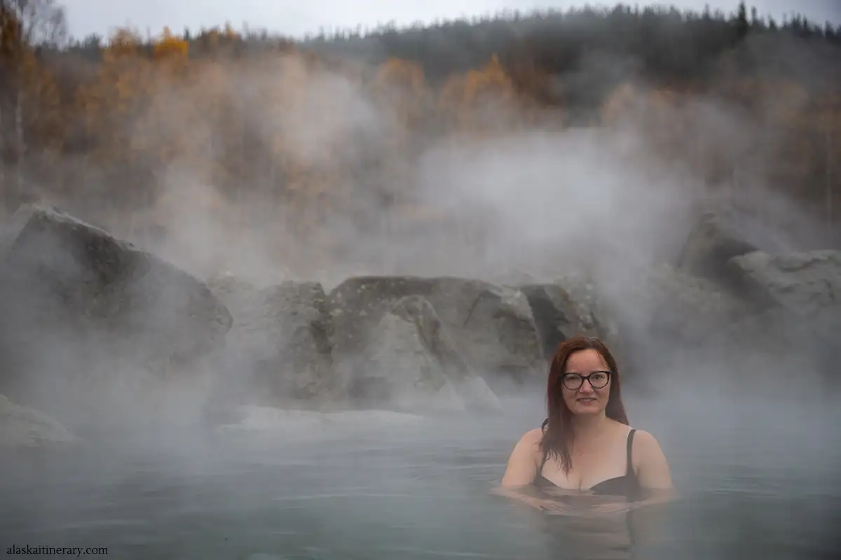 Agnes soaking in Chena Hot Springs with fall colors with a backdrop.