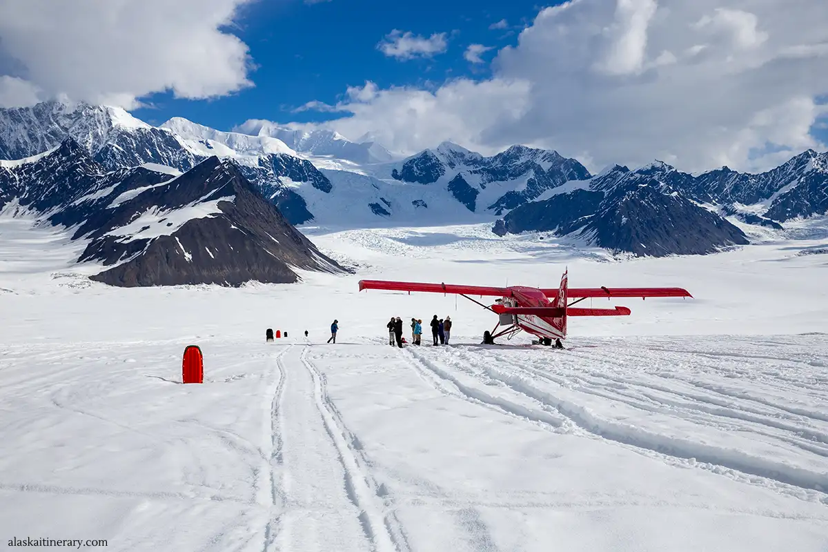 red plane on glacier surronded by mountains peaks during scenic flight tour over Denali with glacier landing.