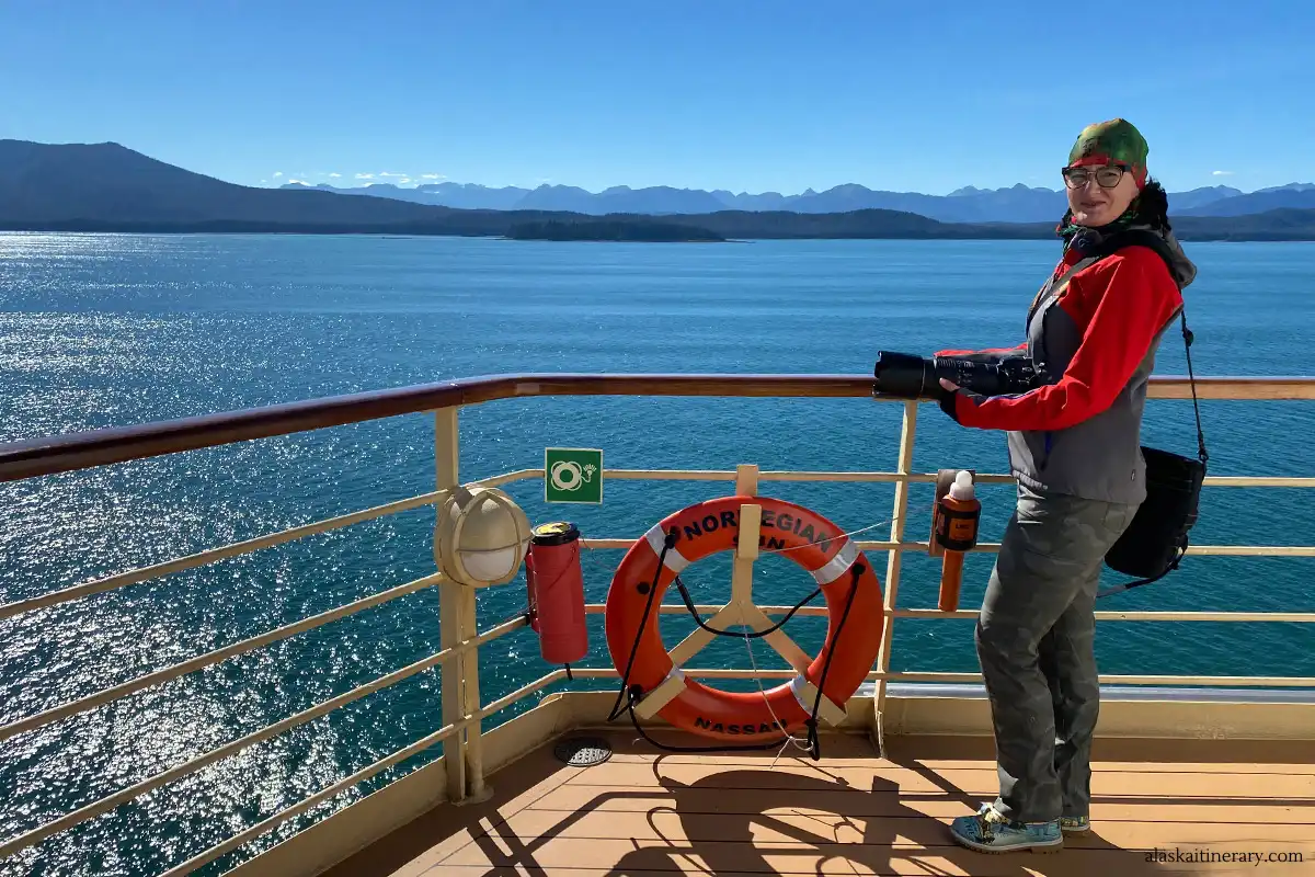 Agnes with her camera on Norwegian Sun ship during sunny day on Alaska cruise with mountains in the backdrop.