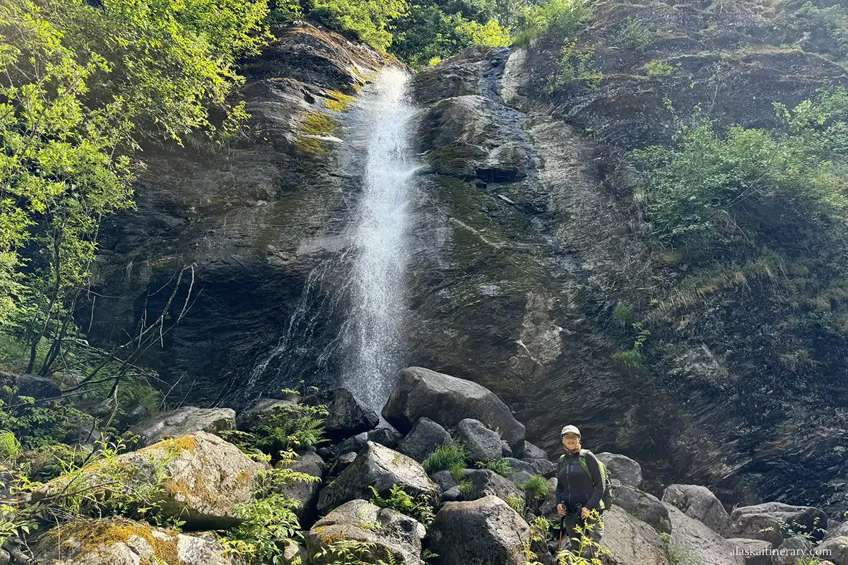 Agnes Stabinska, the author, in Juneau Temperate Rainforest with trees and waterfall in the backdrop.