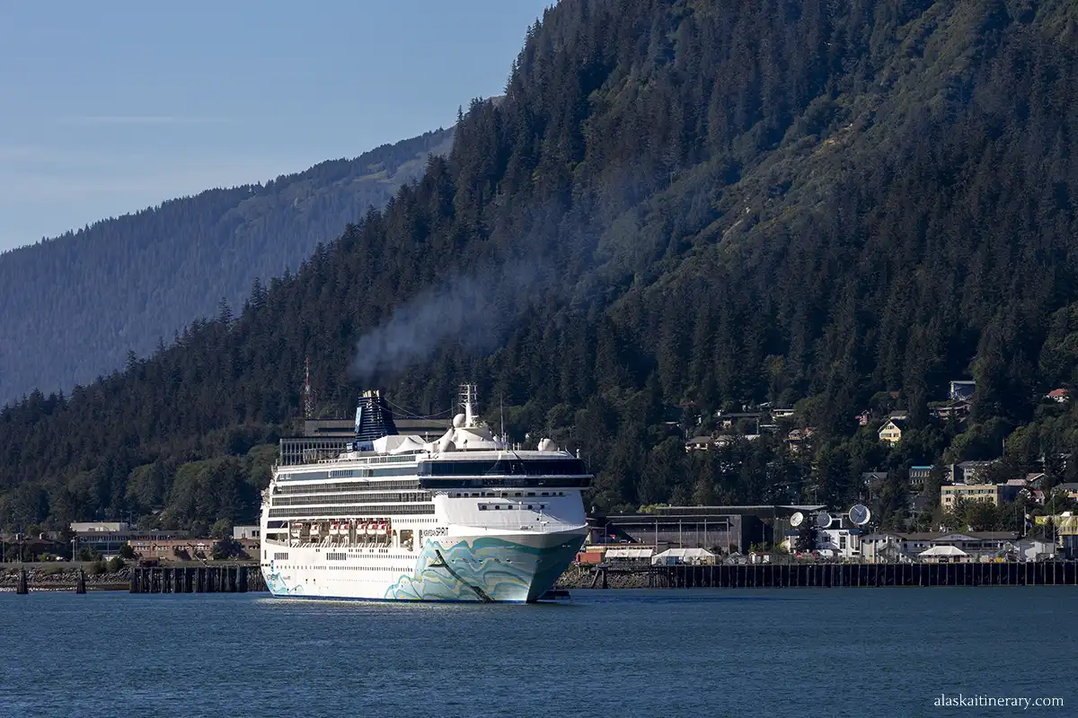 cruise ship in Alaska port with forest and mountain view.