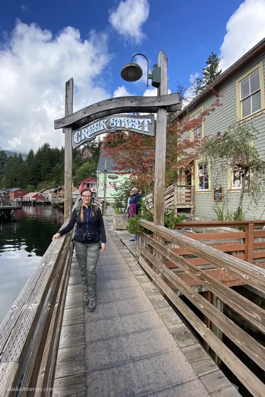 Agnes leans against the railing with the historic wooden Creek Street sign above her head.