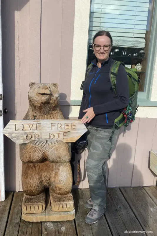 Agnes next to a wooden sculpture of a bear holding a sign with the inscription live free or die.
