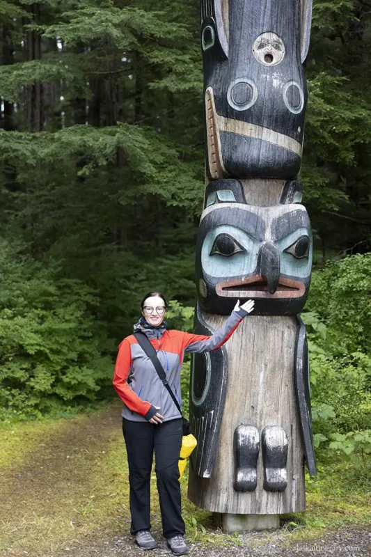 Agnes is standing next to the wooden totem pole carved with birds in Sitka. 