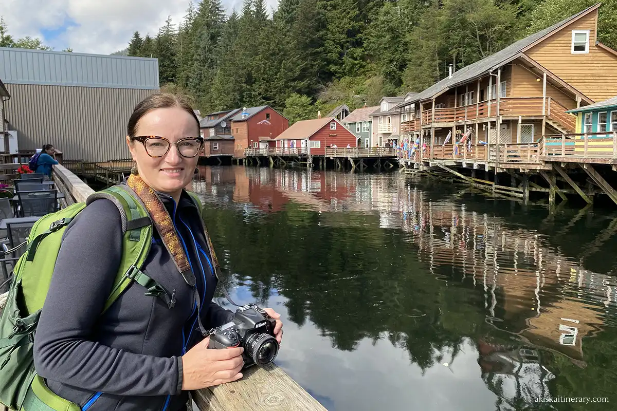 Agnes holds a Nikon camera and takes photos of Creek Street. In the background, greenish water and pastel wooden houses.