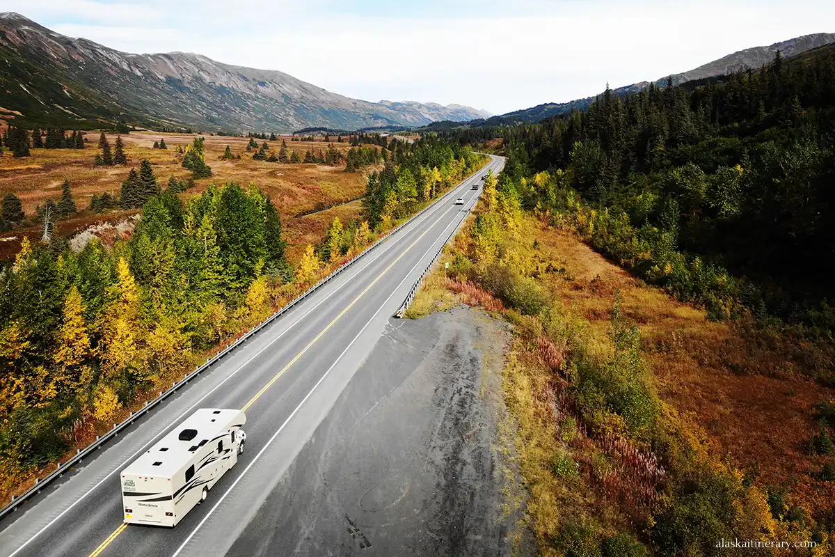 Motorhome cruising on Alaska's Seward Highway amidst fall colors, with vast open landscapes and mountain ranges in the distance.