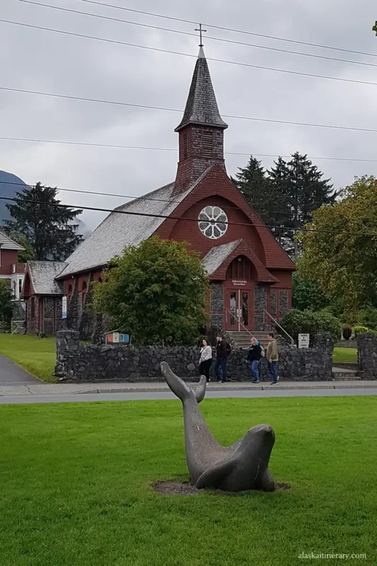 A historic church in downtown Sitka and a piece of park with green grass and a sculpture of a seal lying on the grass.