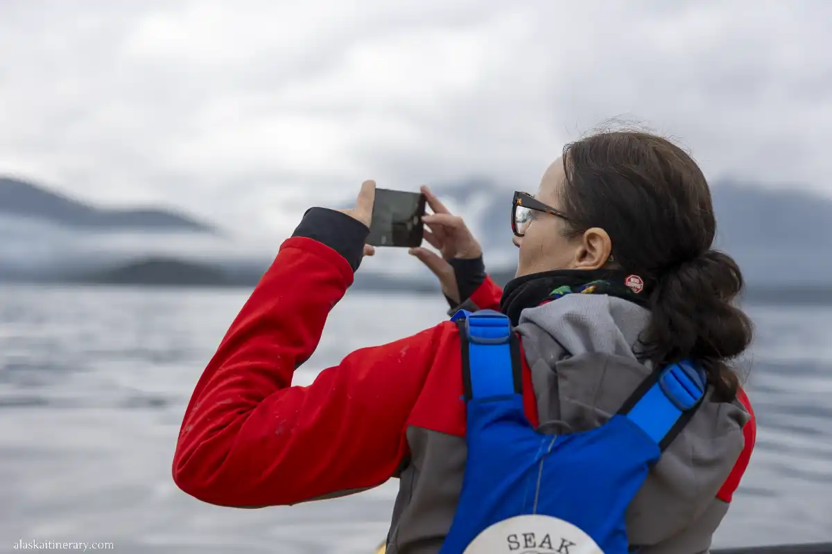 Agnes, the author, is taking a picture of Alaska wildlife using an iPhone 15 Pro Max; she is on a kayak trip during a cruise.
