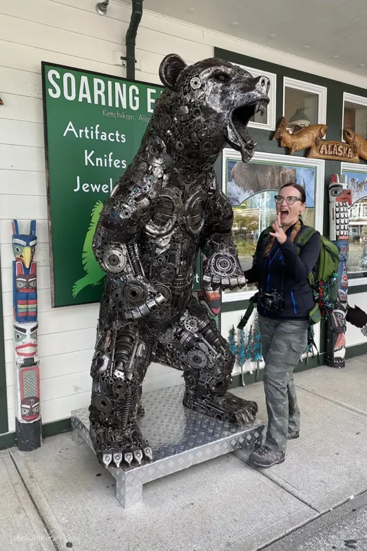 Shopping in downtown Ketchikan, Agnes is standing at the entrance to the souvenir shop in front of which there is a colossal sculpture of a bear.