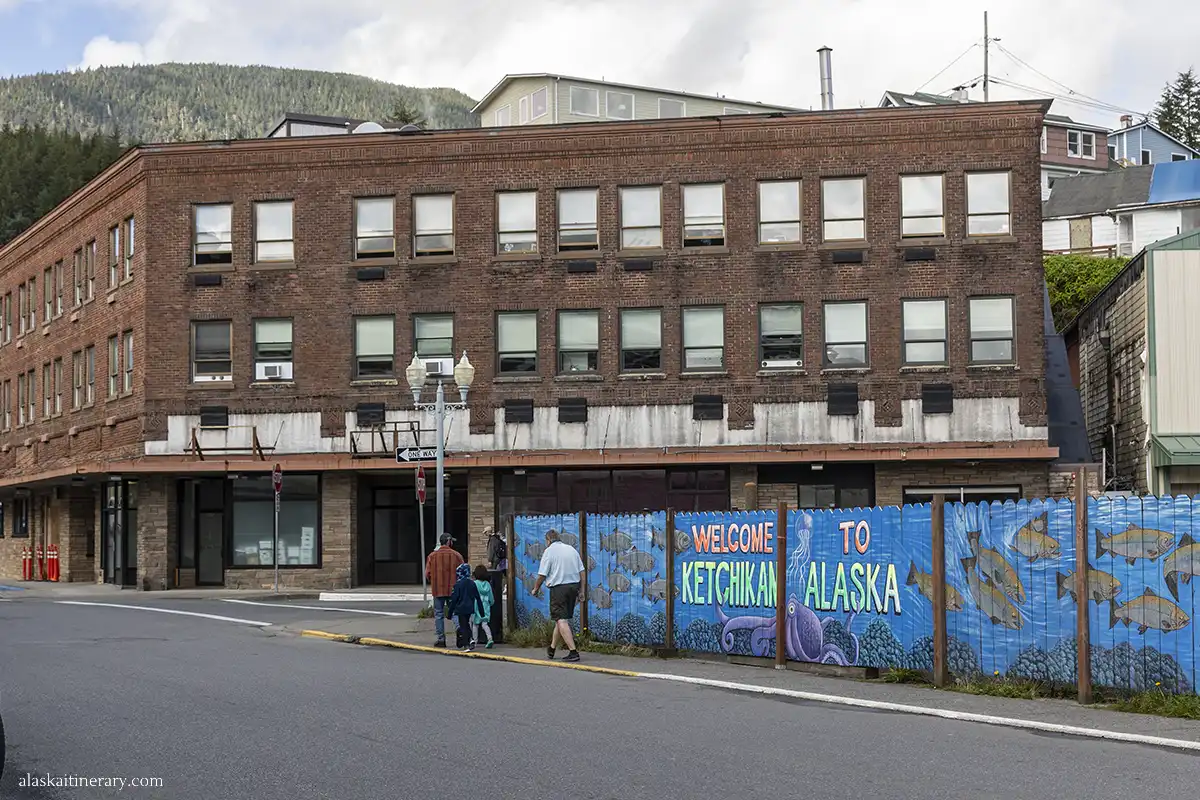 A large building in downtown Ketchikan and the front of it, a mural with colorful fish and the inscription Welcome to Ketchikan.