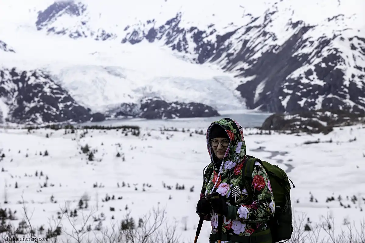 Agnes Stabinska, the author, in warm floral hoodie, with trekking poles and green daypack with the Portage Glacier in the backdrop.