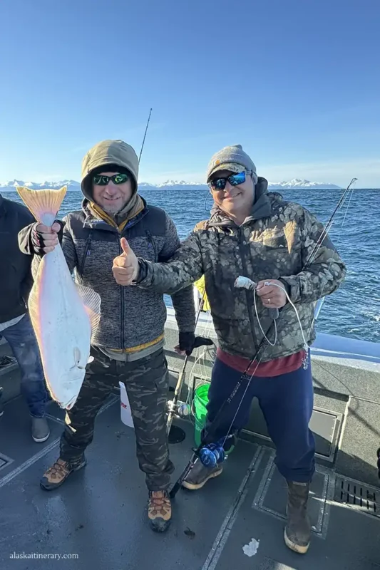 Chris with halibut in his hands next to captain Mike Patterson during halibut fishing trip.