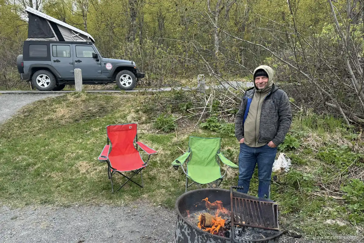 Chris next to campfire and camping chairs on the campground.