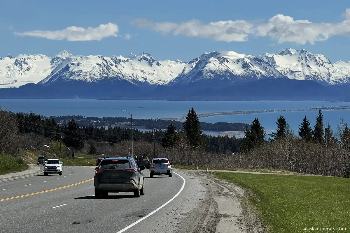 Scenic road trip in Alaska: the route to Homer with the Homer Spit, mountains, sea, and glacier ahead of cars.