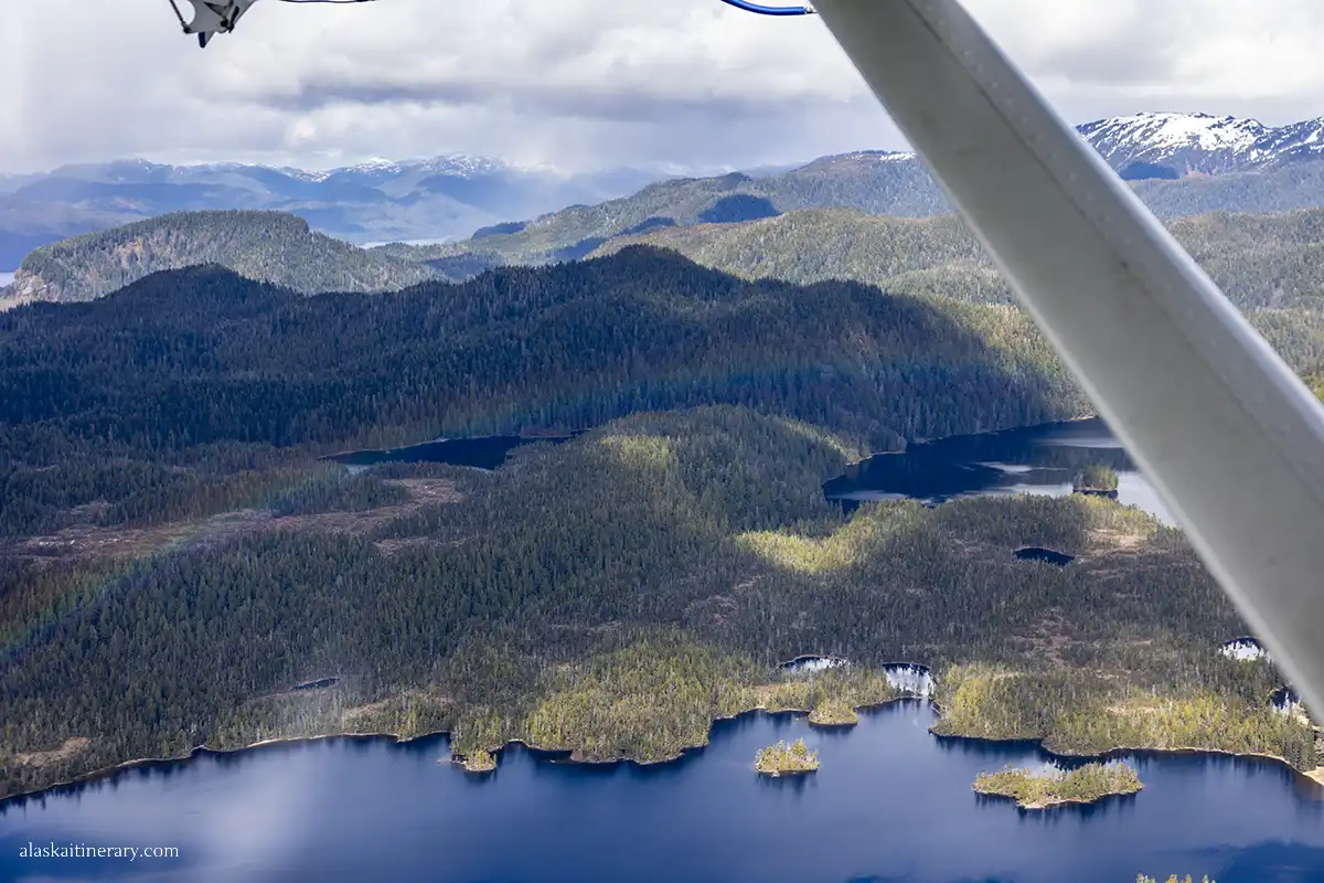 Deep blue water, mountains, forests and rainbow above trees - the view from floatplane.