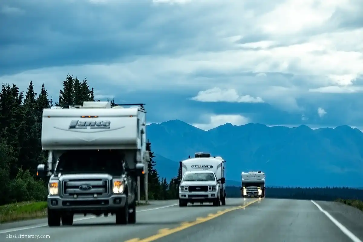 Three large RVs on Alaska road with mountains in the backdrop.