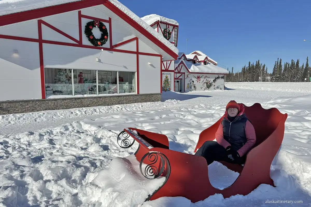 Agnes Stabinska, the author, sits on a sleigh in a winter setting in front of Santa's house in North Pole.